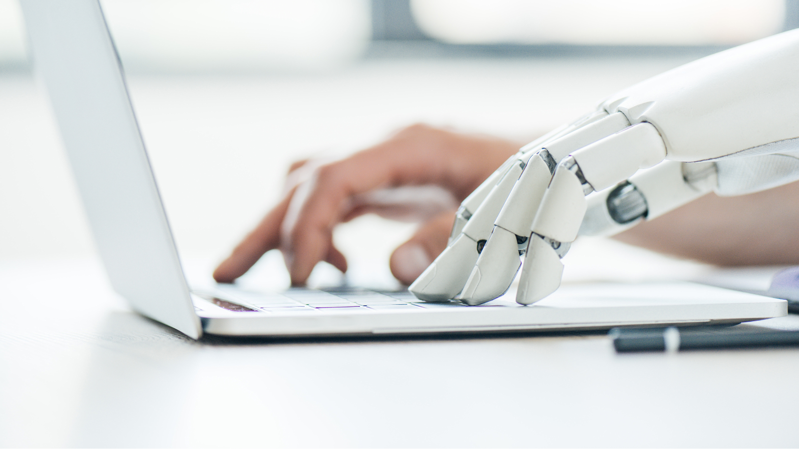 A robot hand and a human hand working together, typing on a laptop. Representing harmony between man and machine.
