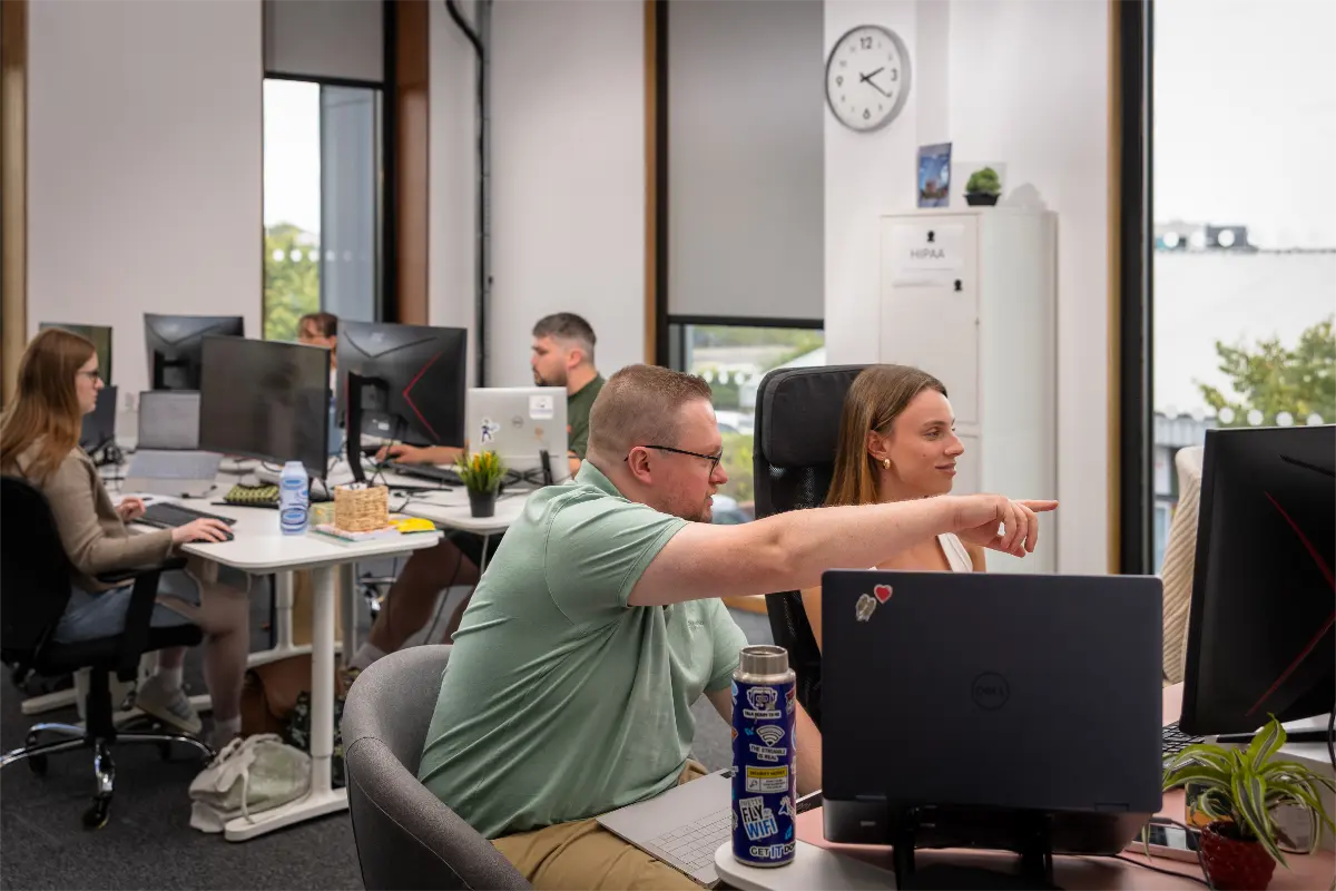 Dave pointing towards Megan's screen helping out with copywriters in background