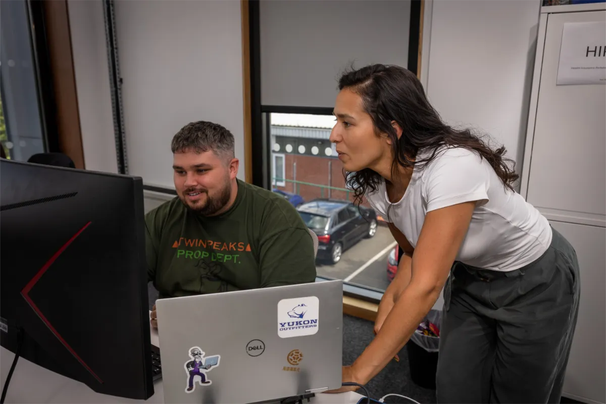 Silvia talking to Luke at desk about upcoming campaign