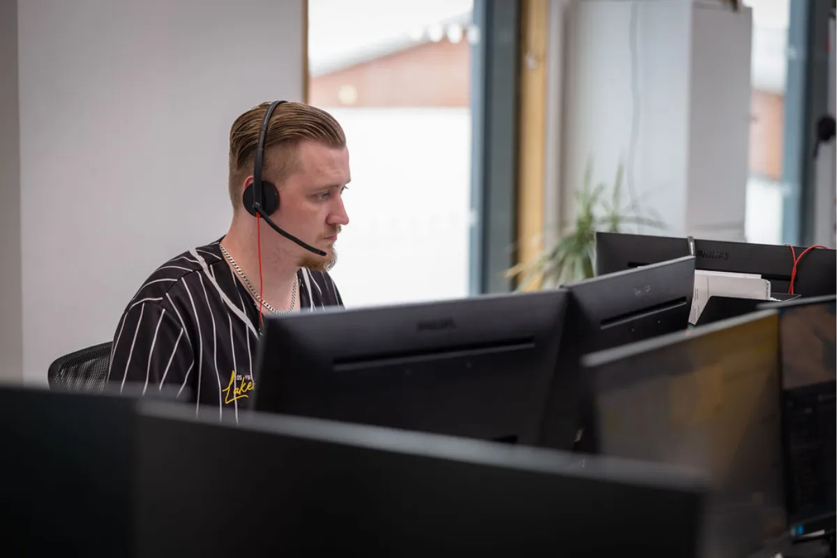 Tom sat at desk in telesales office with headset on call to prospects