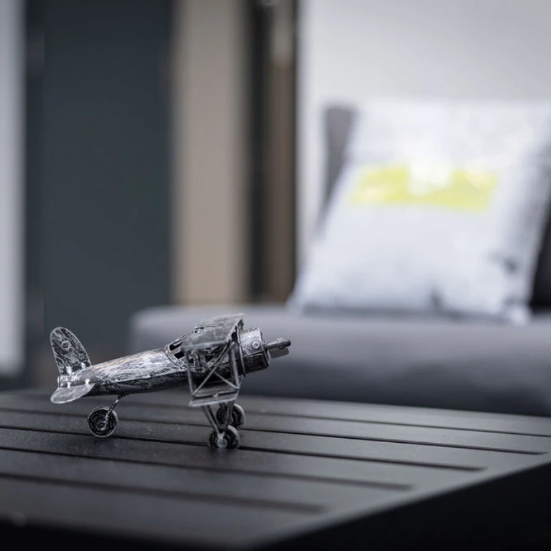 Metal model airplane on a dark coffee table with a blurred sofa and cushion in the background
